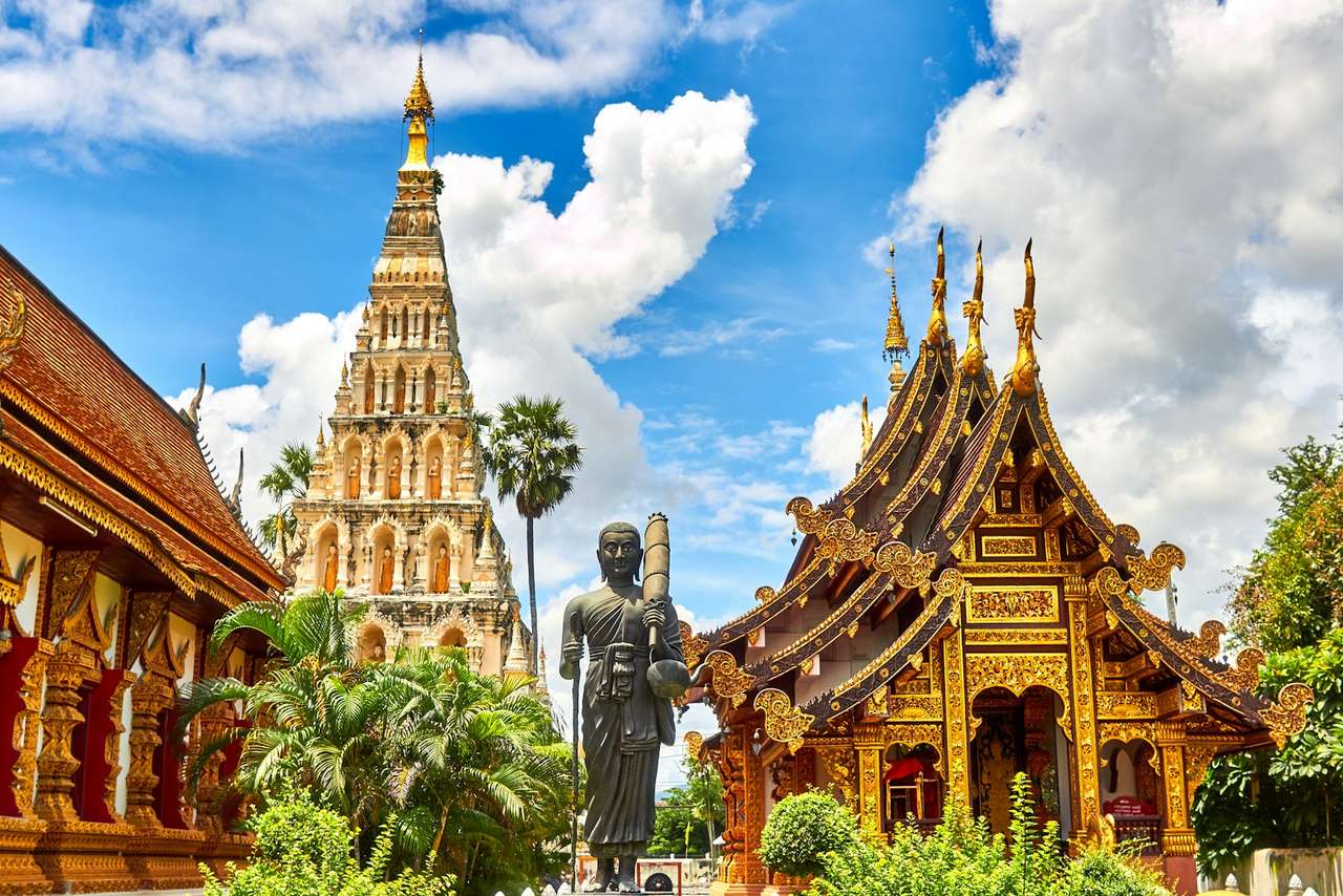 Golden Thai temple spires and a Buddha statue under a bright blue sky, Thailand